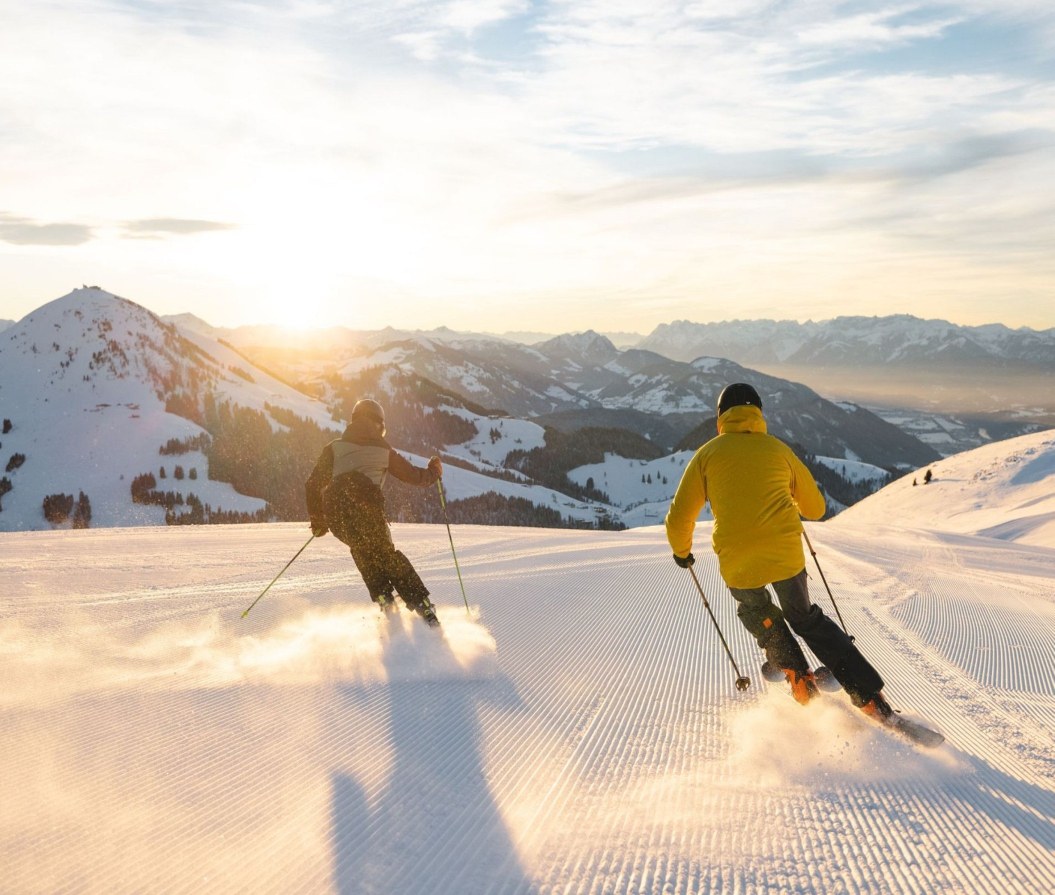 Zwei Skifahrer auf der Piste bei Sonnenaufgang
